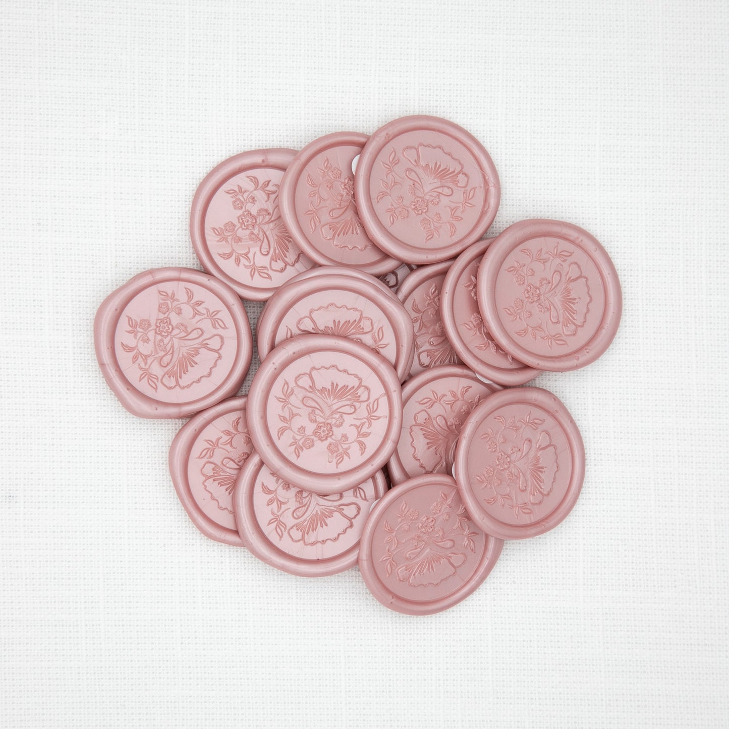 Pink wax seals with floral designs on a white linen background