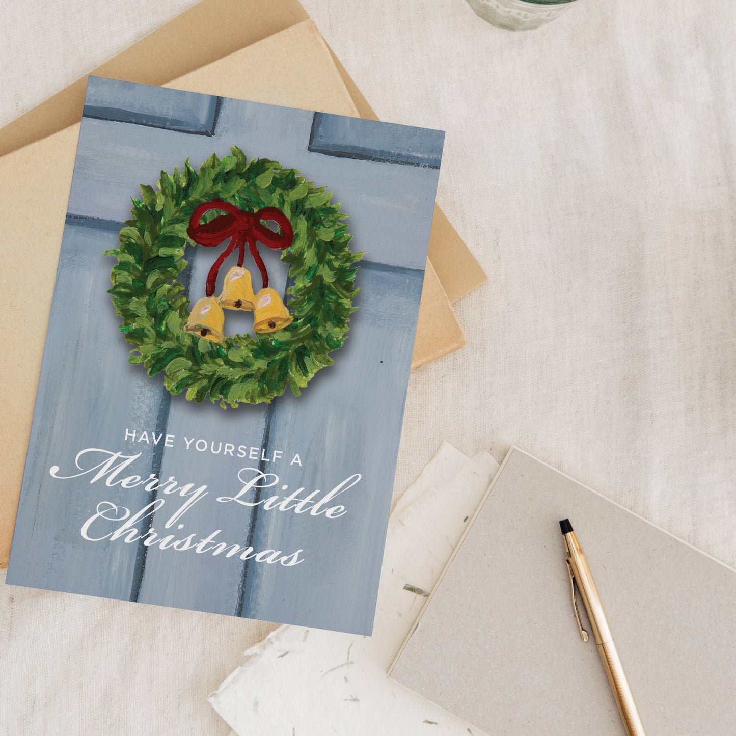 Christmas card with wreath design on a table with a pen and glass.