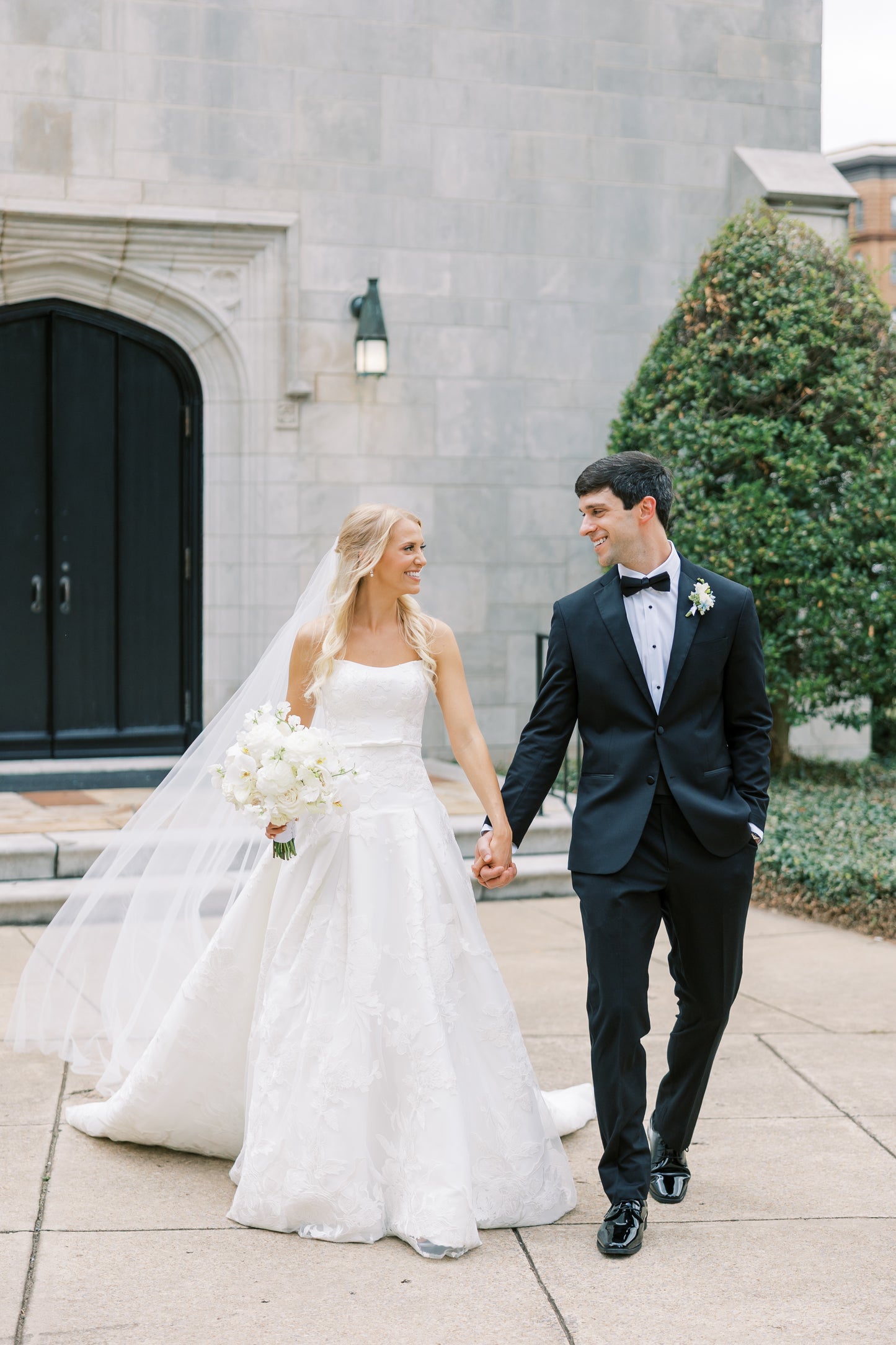 Wedding couple walking hand in hand in front of a stone building.