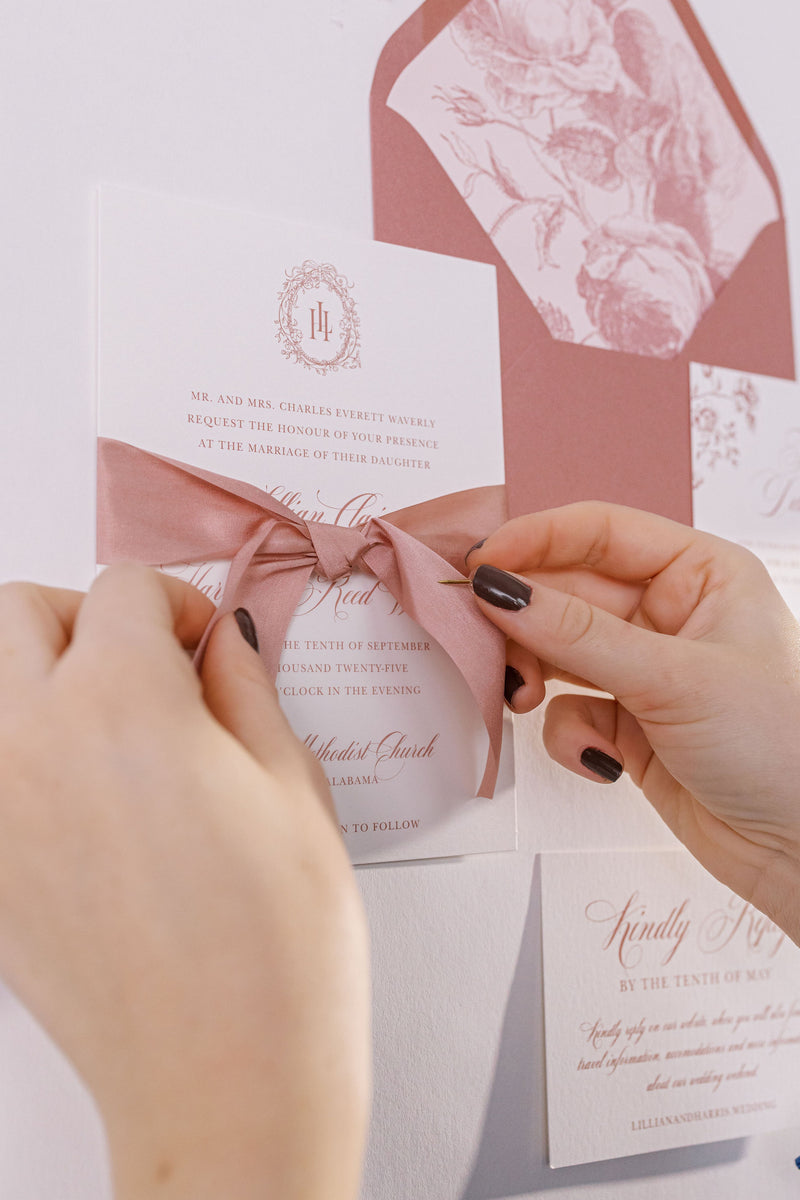 Person tying a pink ribbon on a wedding invitation with floral design
