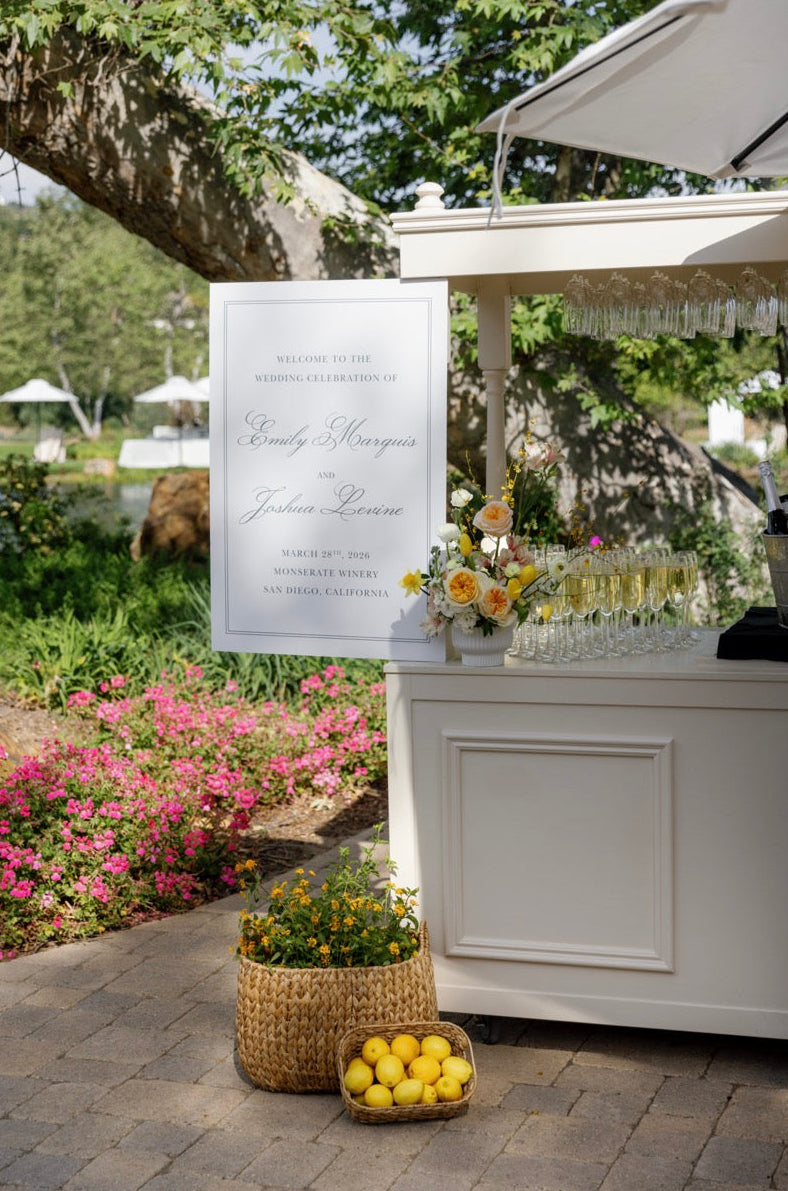 Outdoor event setup with a bar, flowers, and a sign in a garden.